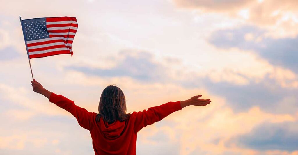 Amerikan bayrağı tutan kadın kolları açık gökyüzüne bakıyor, vatandaşlık avukatı